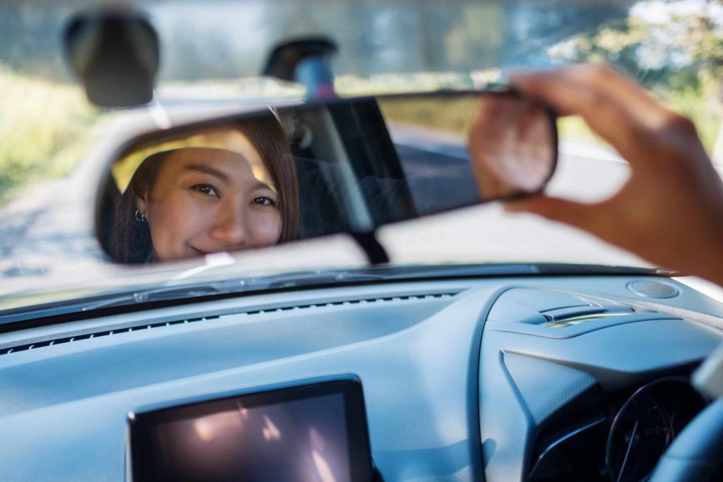 woman adjusting rear view mirror smiling because the money she is saving with her Good Driver Reward Programs