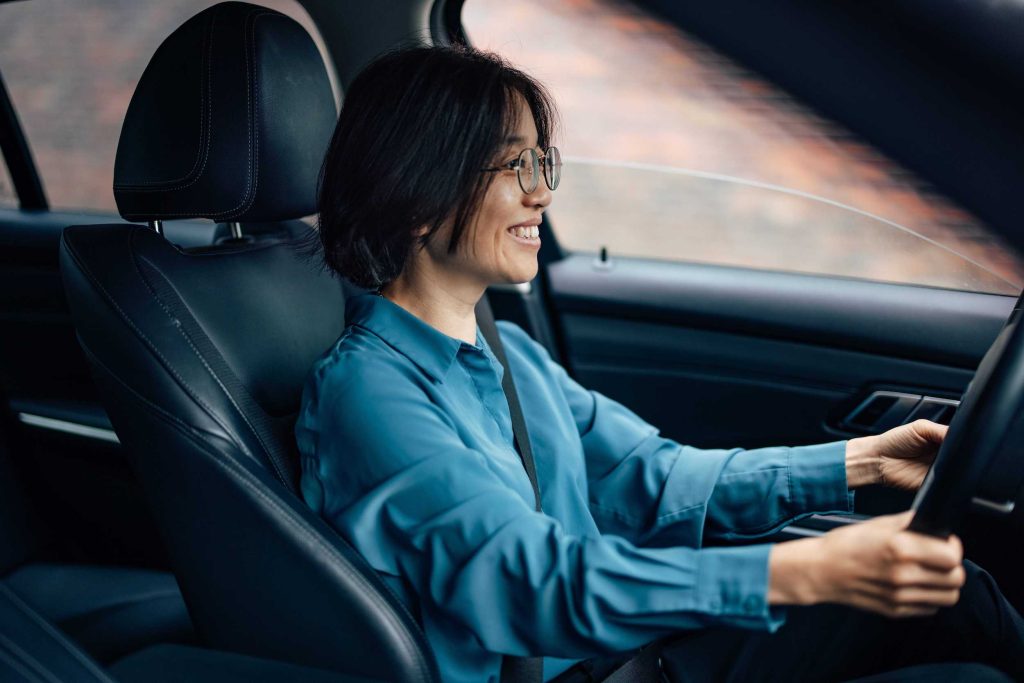 asian woman driving car smiling because the money she is saving with her Good Driver Reward Programs